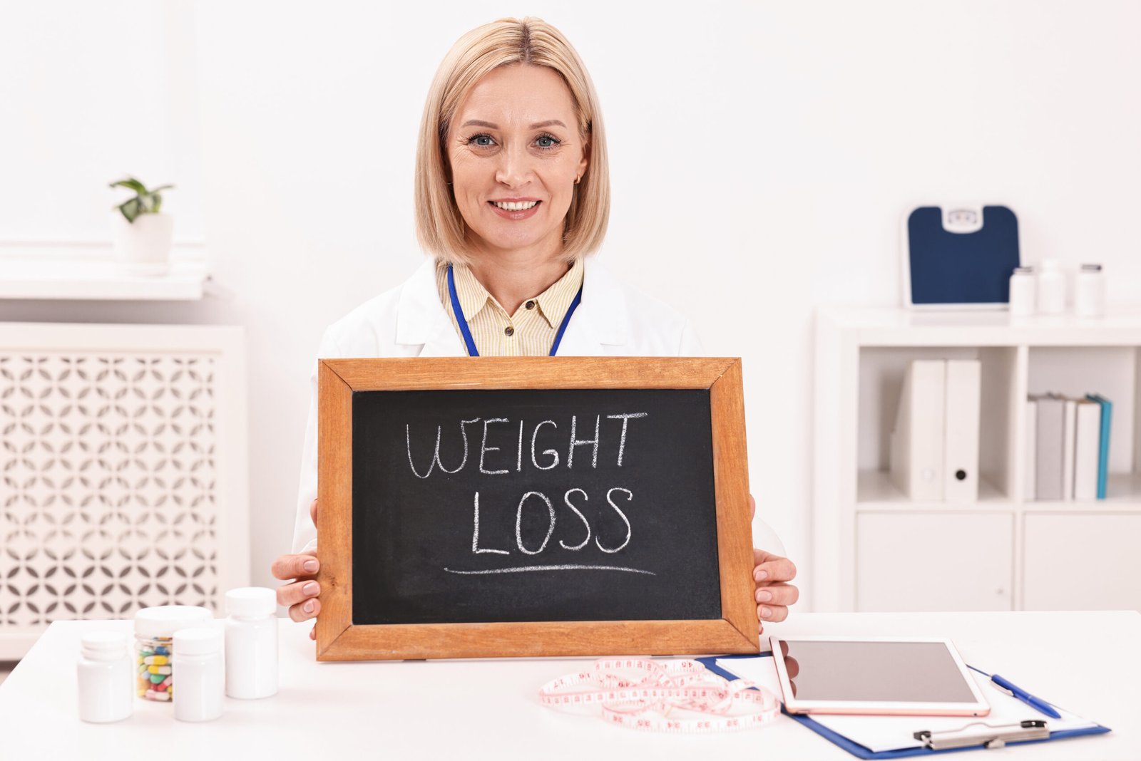 Happy nutritionist holding small blackboard with words Weight loss at table in clinic